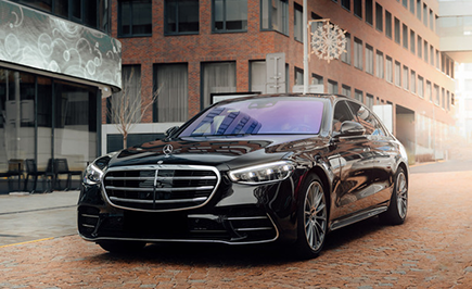 A sleek black luxury car with a shiny finish is parked on a brick-paved street