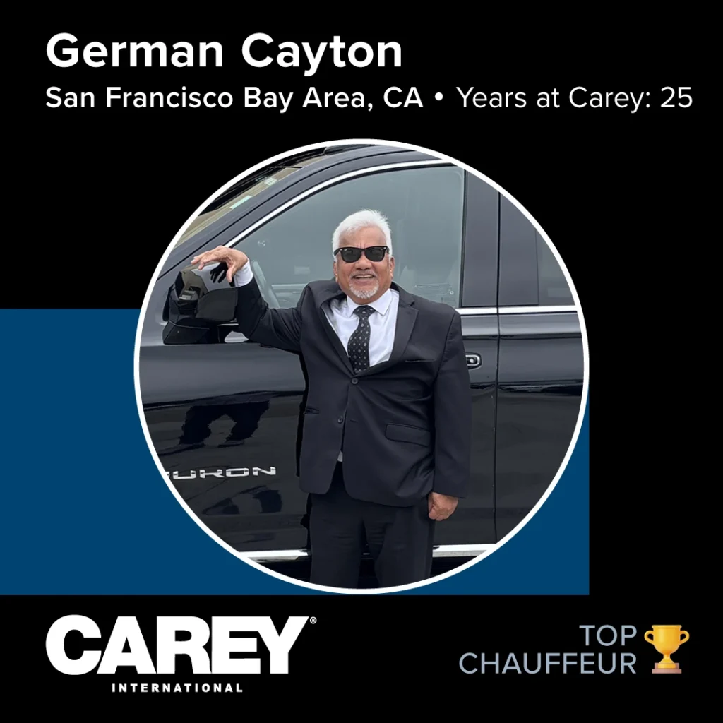 Person with white hair and sunglasses, dressed in a dark suit and tie, standing next to a black Yukon vehicle; award recognition graphics and text present