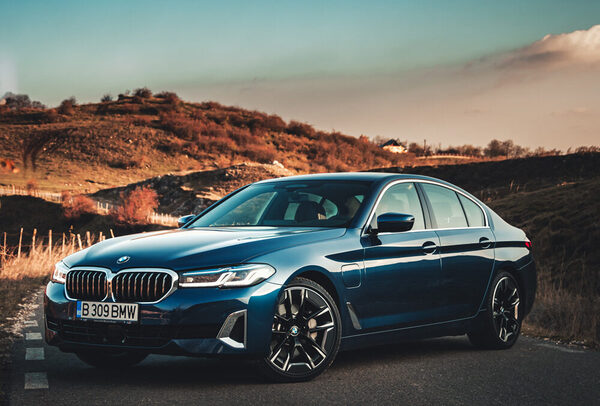 A dark blue BMW sedan is parked on a road with hills and sparse vegetation