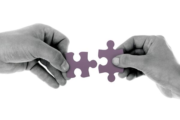 Two hands connecting puzzle pieces in black and white
