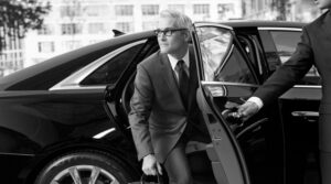 professional stepping out of a luxury sedan, with a chauffeur holding the rear door open