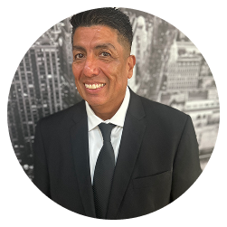 Man wearing a black suit and tie, smiling, posed in front of a grayscale cityscape background inside a circular frame.